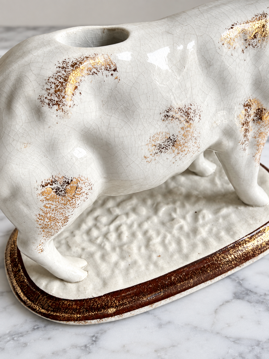 Close-up of vintage ceramic cow creamer showing crazing and worn gilt decoration, edited image
