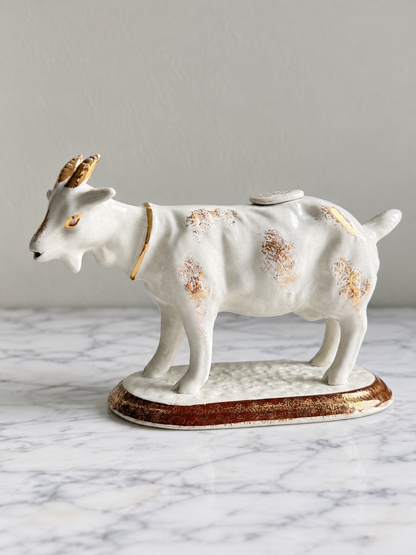Vintage white ceramic cow creamer with worn gold accents, edited side view